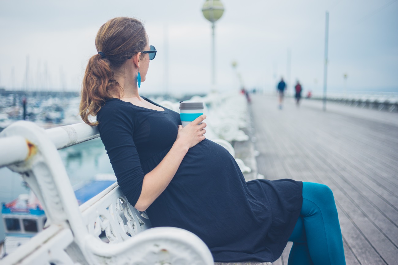 Mulher grávida bebe café em pier durante viagem ao exterior